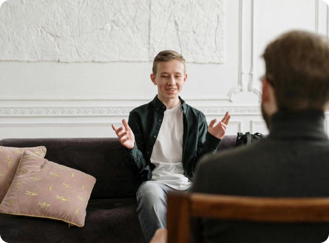 A man sitting on top of a couch talking to another person.